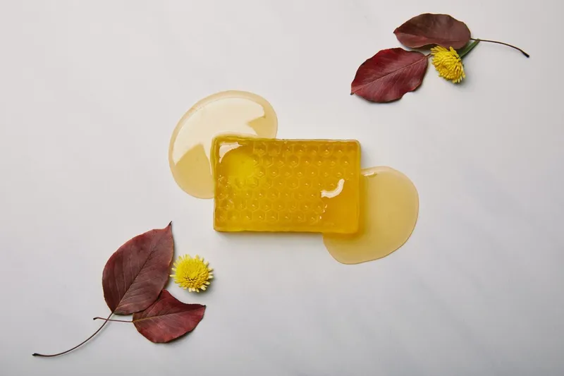 Sản phẩm top view of handmade soap in shape of honeycomb with dandelions and leaves on white marble surface — Mật Ong Hoa Bốn Mùa - Hộ Kinh Doanh Cơ Sở Mật Ong Hoa Bốn Mùa — MST 0101406750