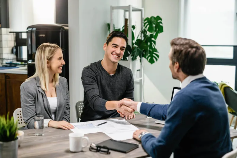 Sản phẩm young happy couple making agreement with their financial advisor home men are shaking hands 1 — Công Ty TNHH Vietnam Global Consulting — MST 0312424893
